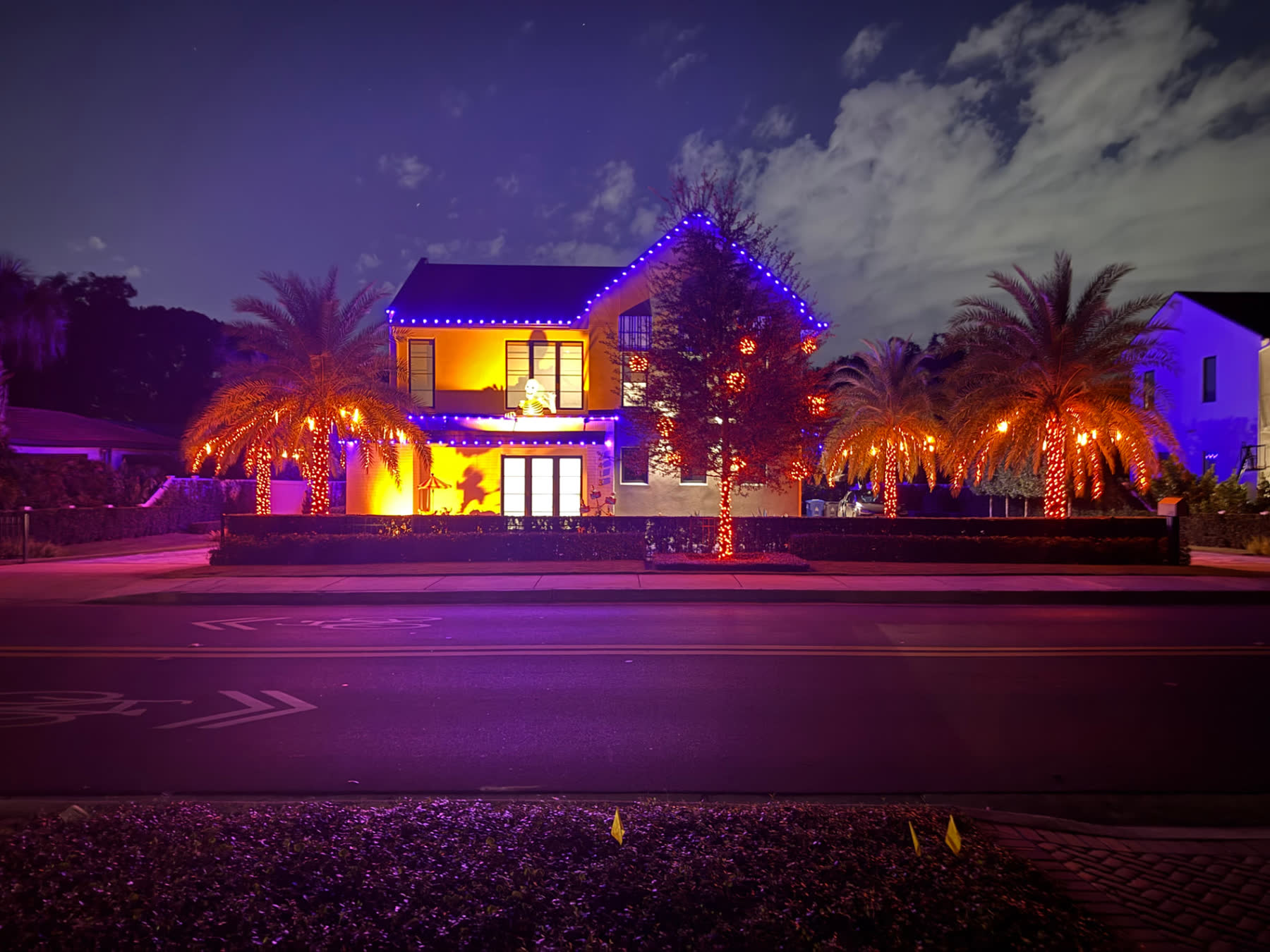 The same Central Florida home lit for Halloween — purple roofline and orange-lit palms from the street